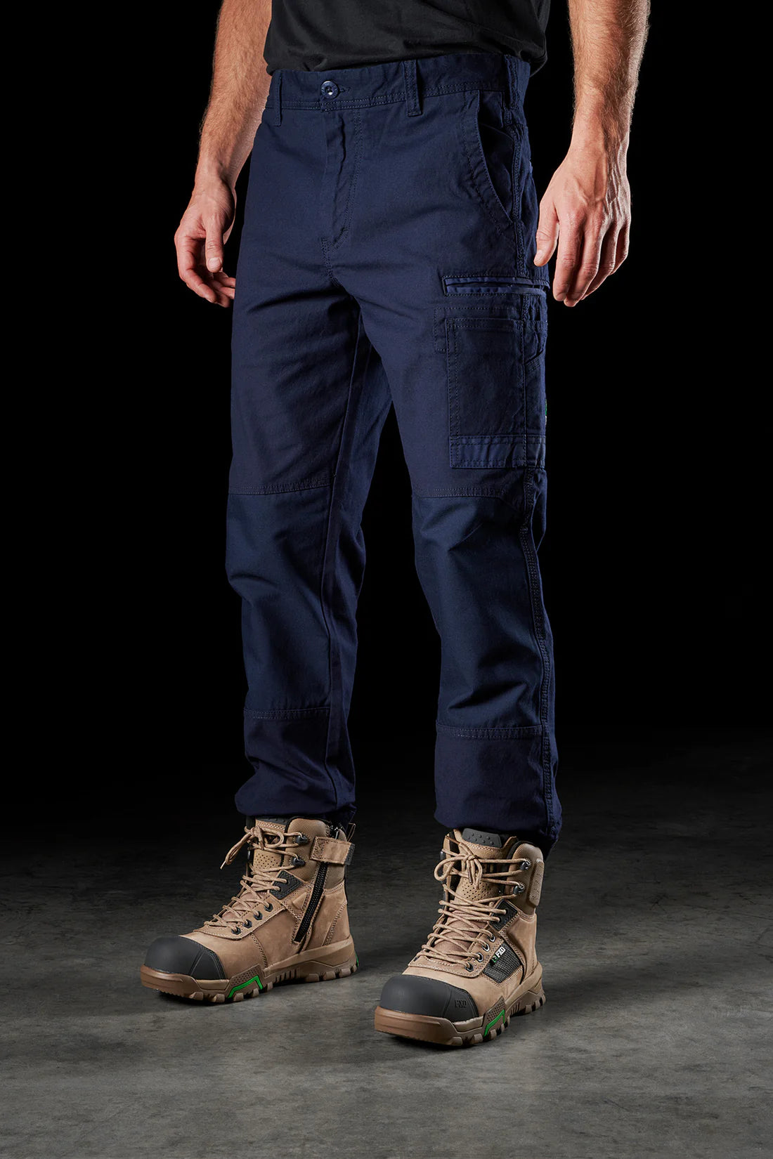 A person standing wearing FXD WP-3 stretch work pants in navy, paired with brown work boots.