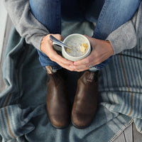 Top down view of woman with boots on holding a mug of soup