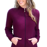 Female model wearing Lothlorian full zip possum merino jacket in Berry. The model has her hands in both pockets and the background is a riverbank.