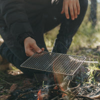 Man placing Alton Goods Ultralight Titanium Grill Small on campfire