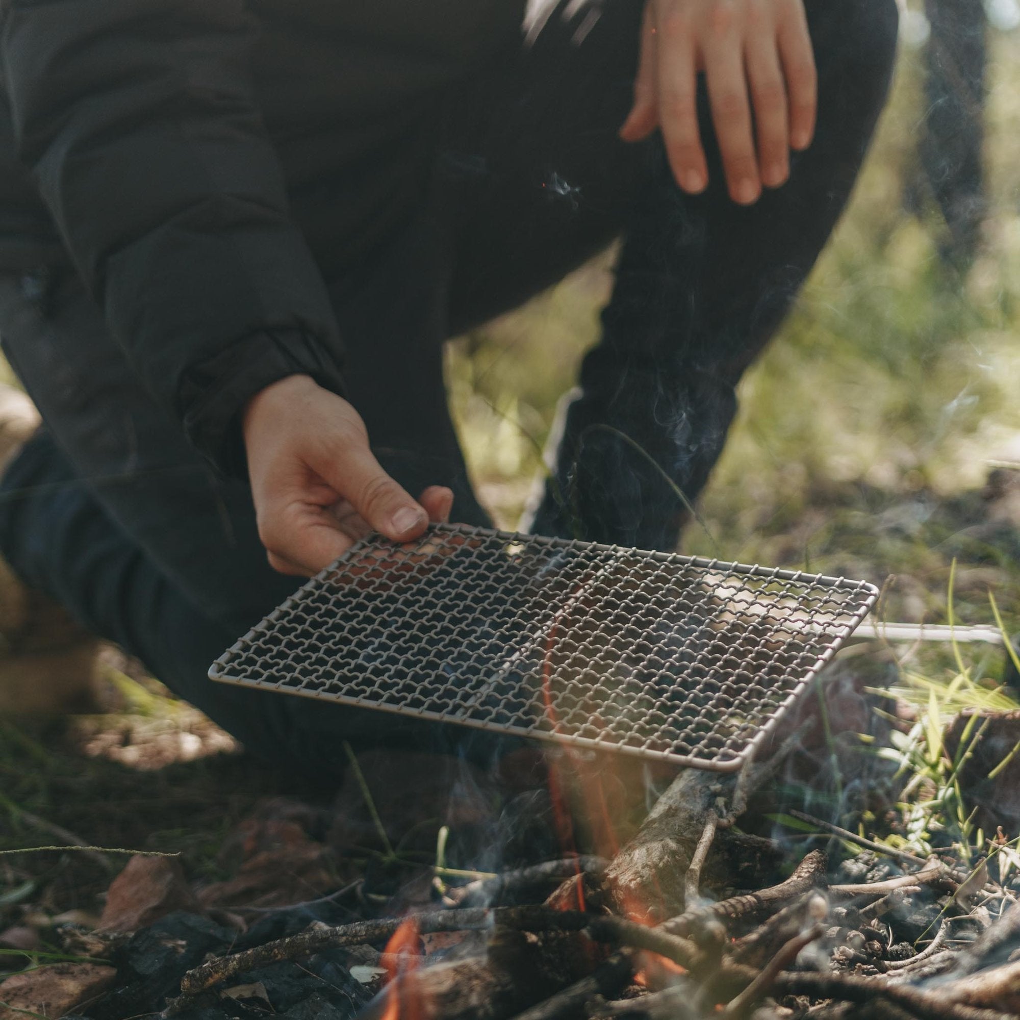 Man placing Alton Goods Ultralight Titanium Grill Small on campfire