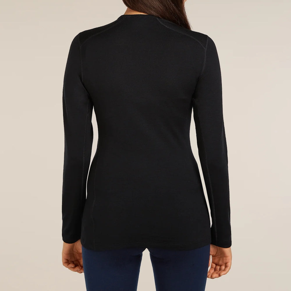 A woman viewed from the back wearing a fitted black long sleeve Icebreaker top and dark blue leggings