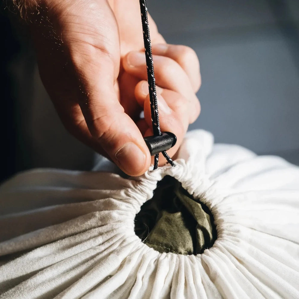 Close-up of a hand tying a drawstring on a white bag