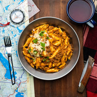 Bowl of Campers Pantry penne bolognese with a map, compass, and mug on a wooden board