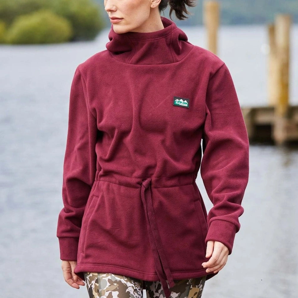 Woman wearing a Ridgeline Saltmarsh fleece jacket in Winter Berry, standing by a body of water.