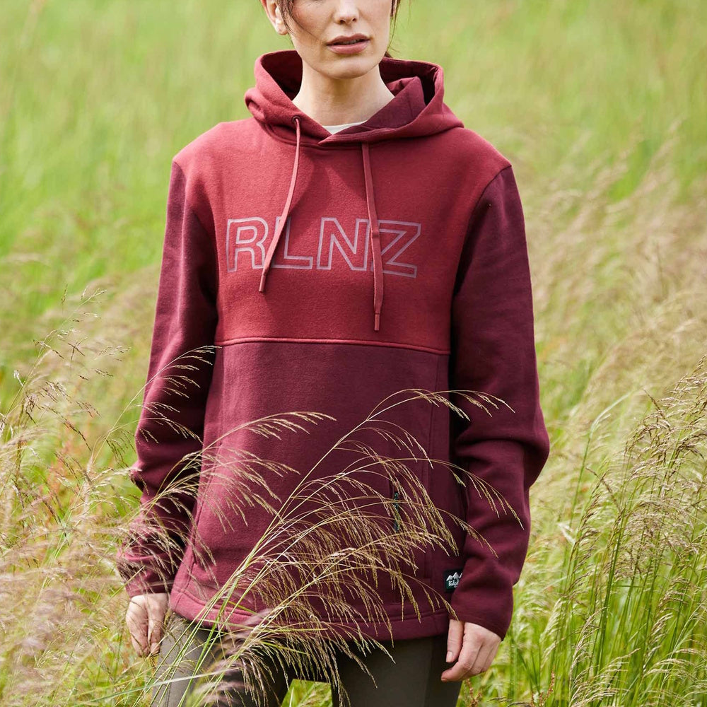 Woman wearing a burgundy hoodie with 'RLNZ' logo in a grassy field