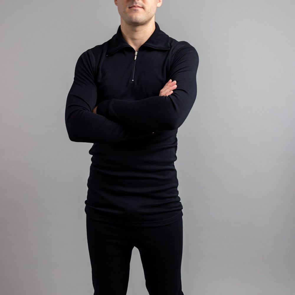 A man wearing a black Icebreaker long-sleeve quarter zip thermal top and black leggings, standing with arms crossed.